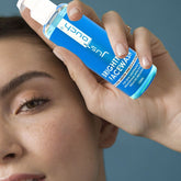 Person holding a bottle of Just Touch Brightening Face Wash near their face against a blue background
